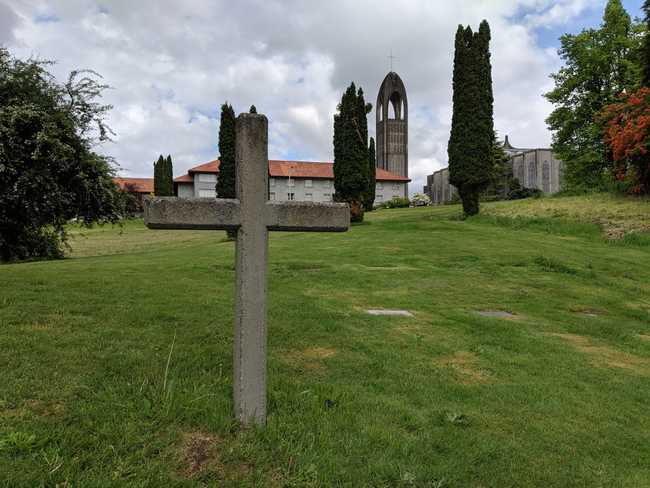 View of a green hillside up to a church. In the foreground is a plain
cross in a graveyard.