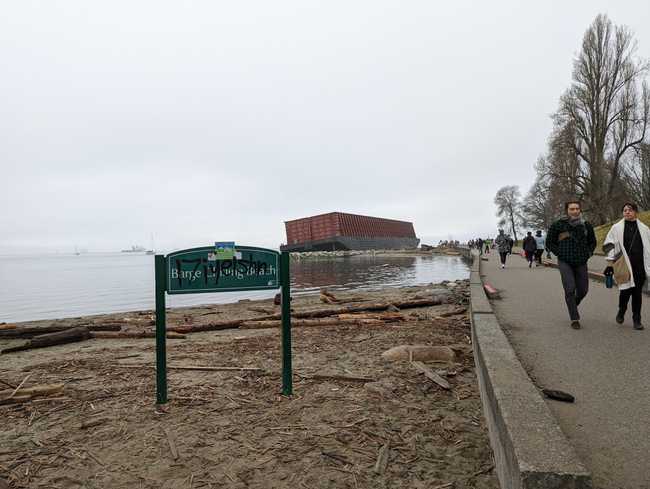 A picture of a bit of beach next to the Vancouver Seawall. In the
background is the barge that washed ashore. On the beach is a joke sign
put up by the Vancouver Park Board. It's grafittied.