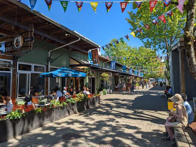 A pedestrian street. One the left is a cafe with a patio. Triangular
flag bunting crisscrosses overhead.