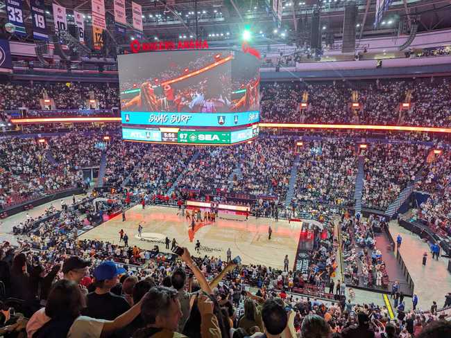 Basketball court. The audience are waving their cellphones back and forth with their flashlights on.