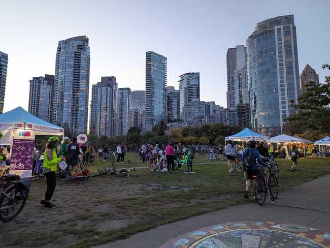 A park with glassy skyscrapers in the background. There are some staging tents, and a lot of people with
bicycles.