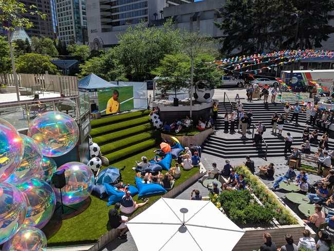 A viewing party from above. There's a lot of stuff going, from giant decorative bubbles on the left, the screen atop
astroturf stairs, and folk sitting around enjoying the sun.
