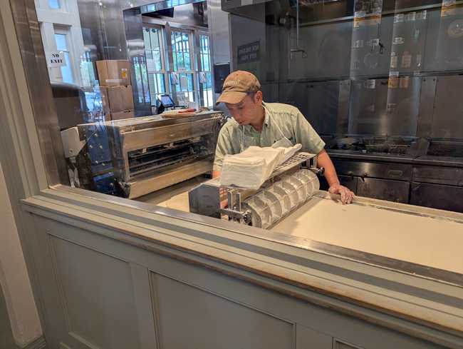 A man working at a machine with a conveyor belt of dough.