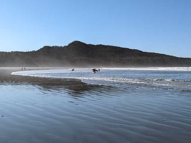 A flat beach with a few ways. Some surfers are walking to the ocean.