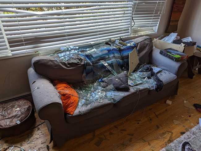 A picture from inside the apartment. The blinds are down, but you can
see leaves on the other side. A grey couch in covered in nasty shards of
glass.