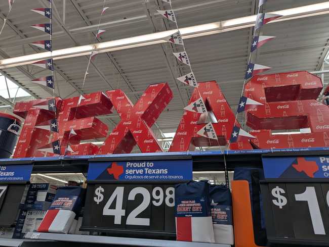 Inside a big box store. "TEXAS" is written in red cardboard boxes with Coke branding.