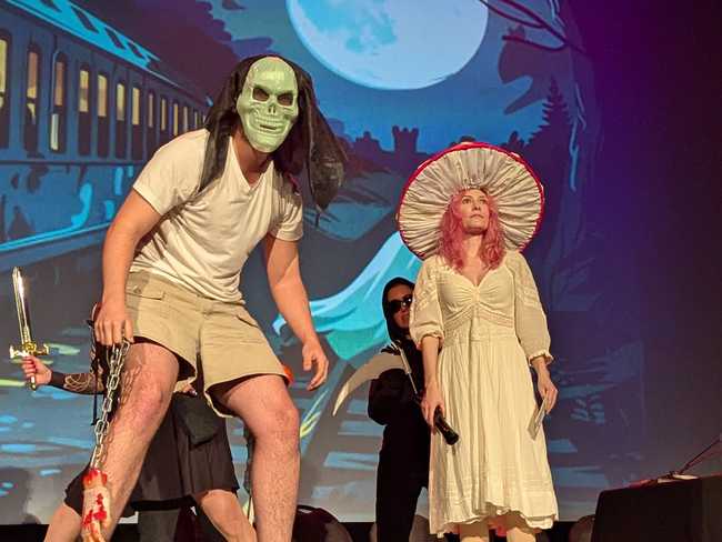 There's a guy in a creepy mask holding a chain with a severed hand at the end. To the right is a woman dressed like a
mushroom.