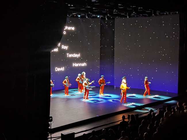The walls have stars like space. The rear wall has names on it, corresponding to the position of the people on stage.
They likewise have their names and a halo on the floor under them, letting you know who everyone is.