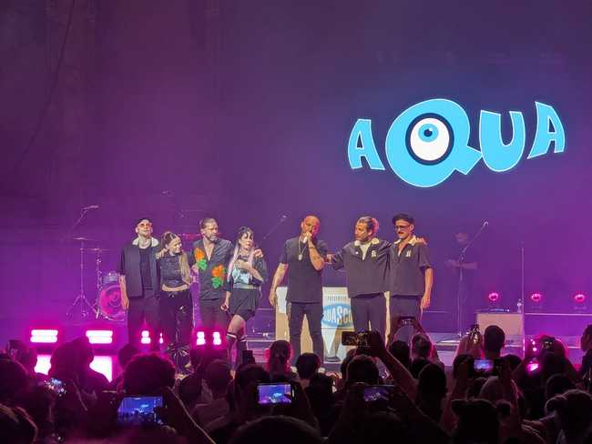 The band and supporting musicians, lined up and talking to the audience.