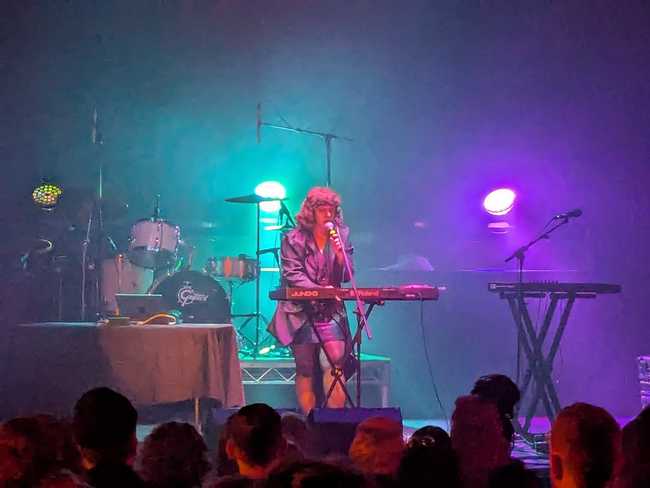 A woman on stage playing keyboard and singing into a mic.