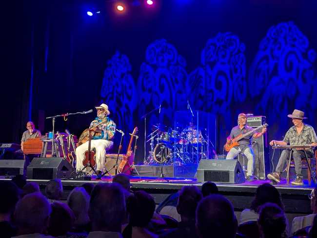 Five men on stage performer. From left to right, there's a piano player, Taj Mahal on guitar, the drummer, a bass
guitar player, and 