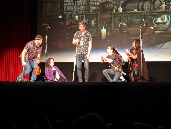 Grainy photo of five people on stage. The guy in the middle is
standing while everyone else takes a knee to listen to
him.