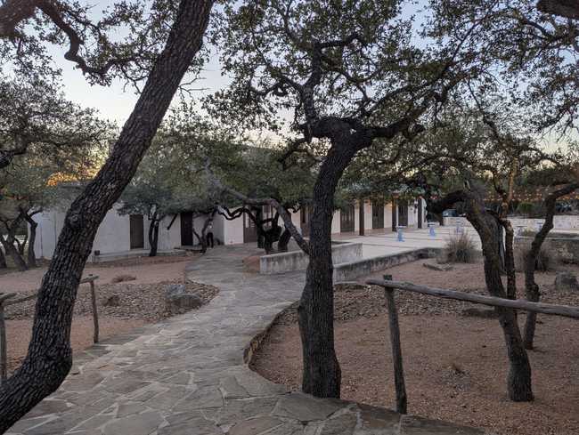 A stone walkway snaking through trees down to a large building.