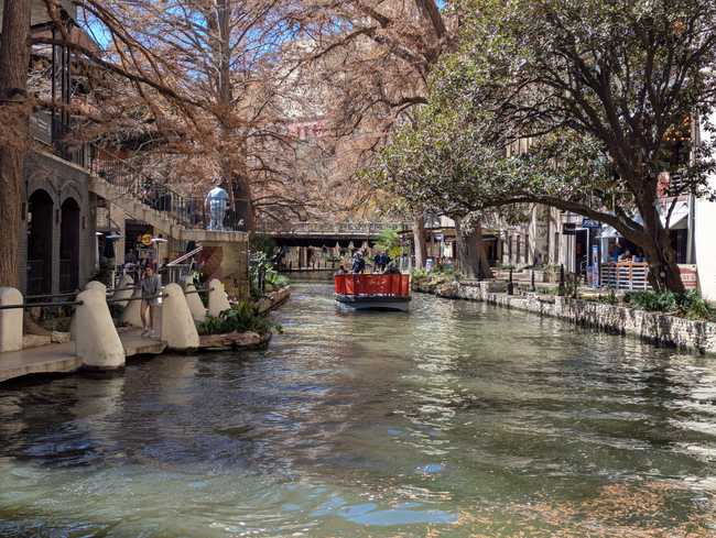 There's a passenger barge on a river. There are pedestrian walkways on either side, a bridge in the distance, and a
tonne of trees.
