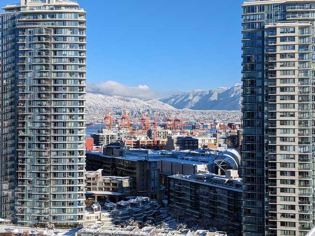 A picture looking towards the mountains. It's framed by glassy
skyscrapers. In the middle are cranes from
the Port of Vancouver.