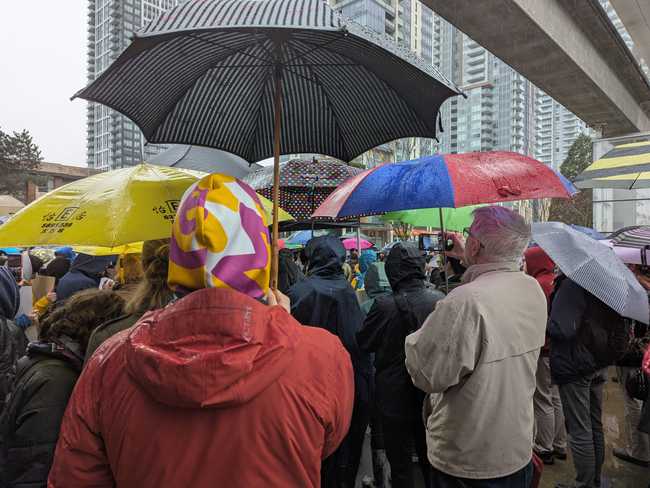 A crowd of people listening to a speaker you can't see because of, y'know, the crowd. Lots of rain gear.