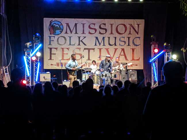 A band performing in front of a banner reading "Mission Folk Music
Festival"