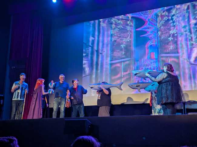 Three audience members with inflated sharks on stage menace the adventuring party, who are all wearing red-blue 3D
glasses.