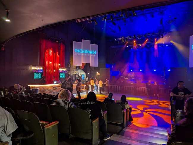 The inside of a club. There are a few rows of movie-theatre seating in front, an empty dance floor, a bar on the left,
and the stage at the back.
