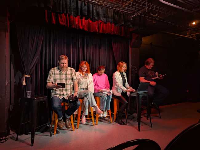 Five performers on stage reading scripts (mostly off phones).