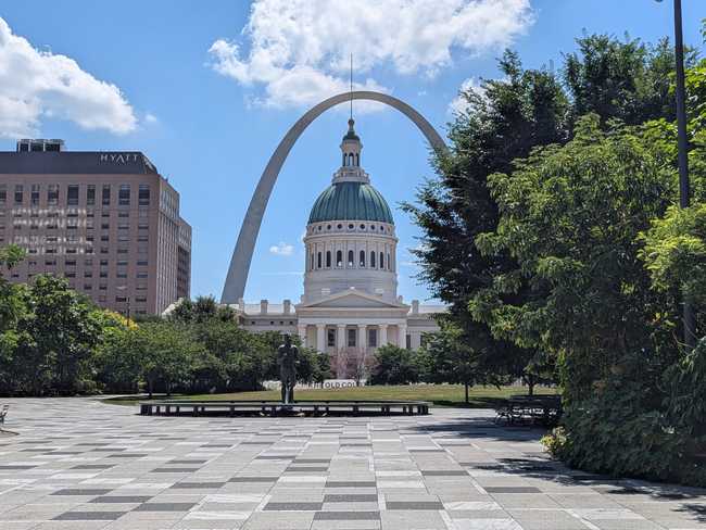 View of Gateway Arch from a park. Under the arch is an impressive domed building.