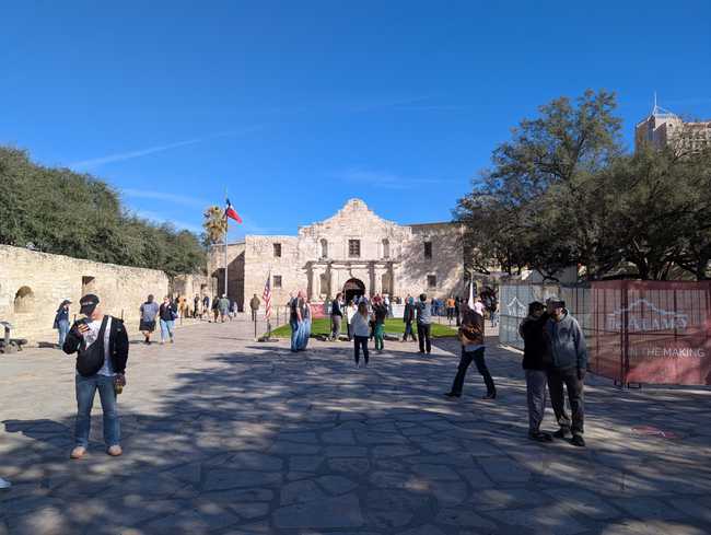 Stone wall on the left; the mission in the distance; and a crowd of tourists in between.