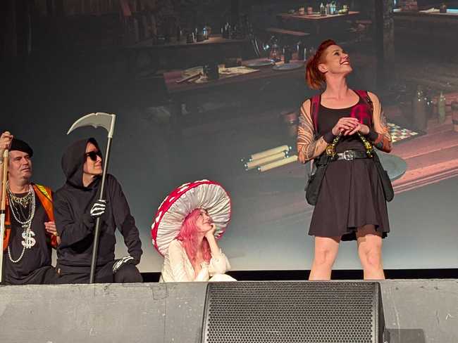 Three of the performers kneel on the left, listening to a woman on the right.
