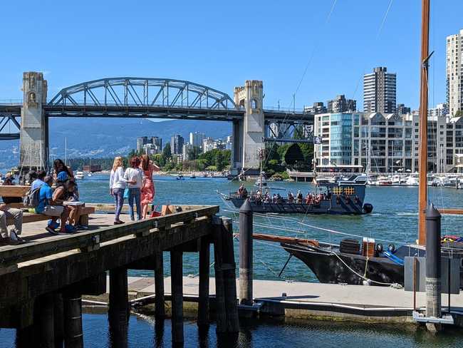 A picture of an inlet. In the foreground are some people standing on a
pier. In the water is a tourist pirate ship. In the background is a
large bridge, which crosses the water and connects to
downtown.