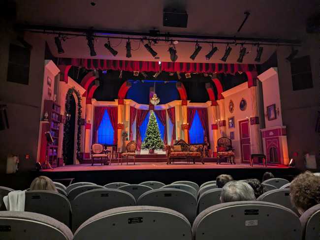 The inside of Metro Theatre. The stage is configured to look like a living room for Christmas, with couches, chairs, and a big Christmas
tree in the back.