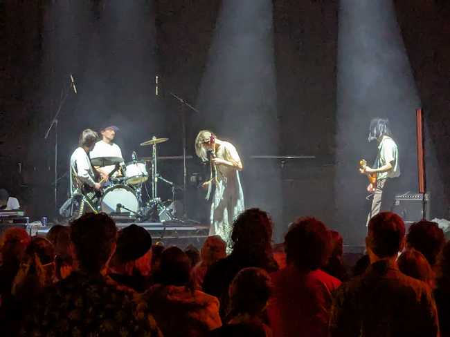 The band on stage under white spotlights, in front of a crowd lit up blood red.