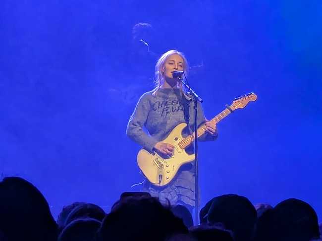 A zoomed in picture of the front-woman. She's playing guitar and singing.