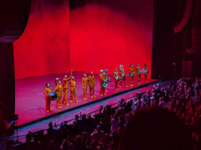 The stage is lit red. Everyone is in a row, taking in the applause.