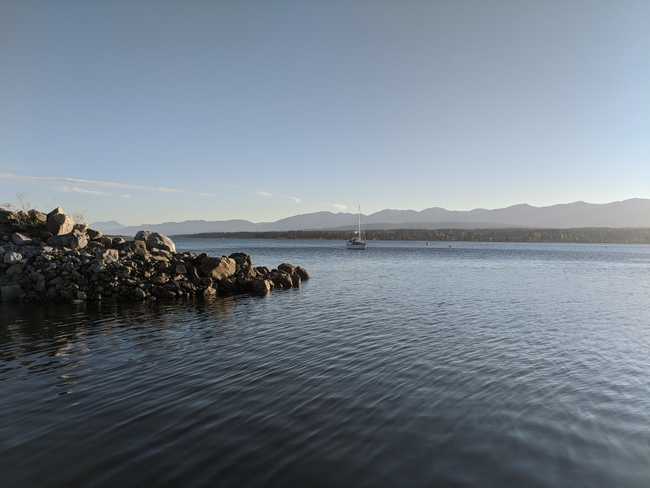 Ocean view with a breakwater on the left. Distant mountains. A
sailboat in the distance.