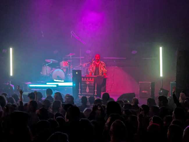 A closer picture of Devours in front of the audience, with neon blue and pink lighting.
