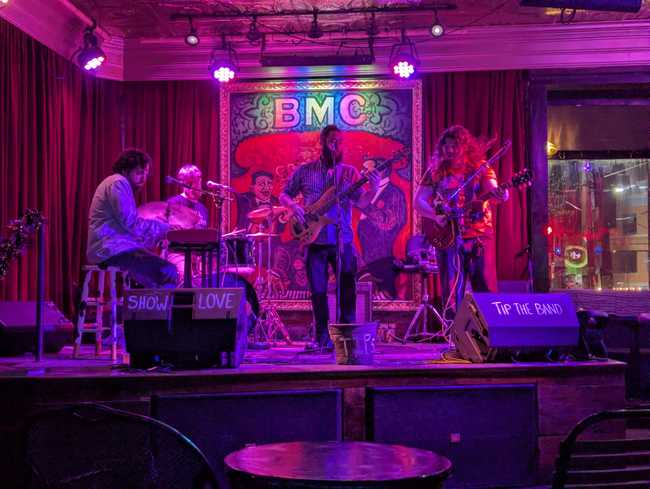 A four piece band playing rock music under pink lights.