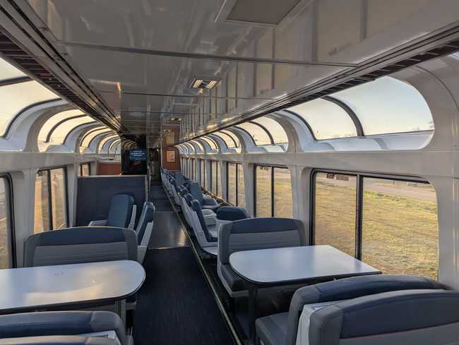 Inside a train car. Either side has windows going up to the ceiling. There are booths with tables for folk to hang
out.